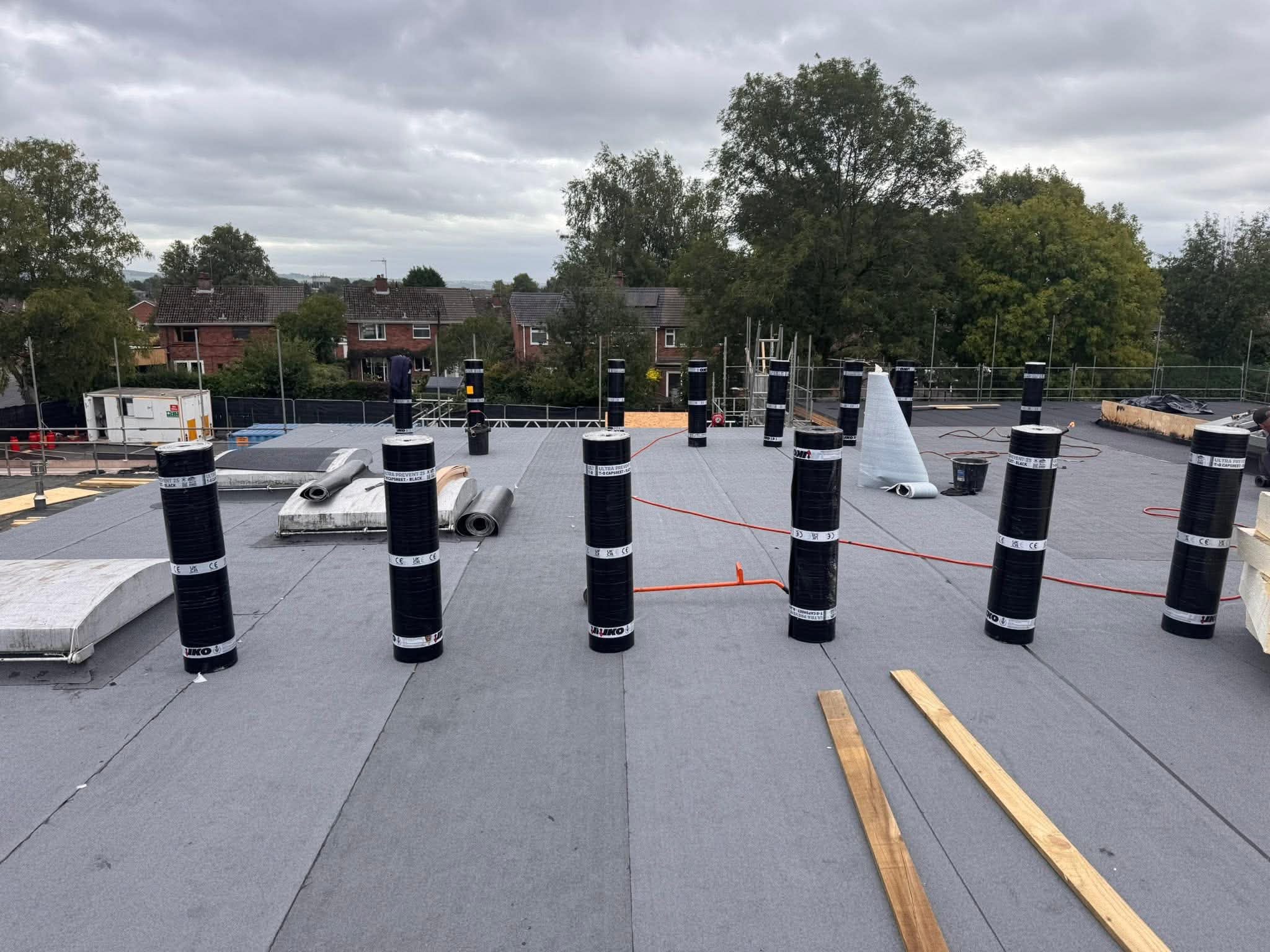 Rolls of capsheet felt staged across a large commercial flat roof