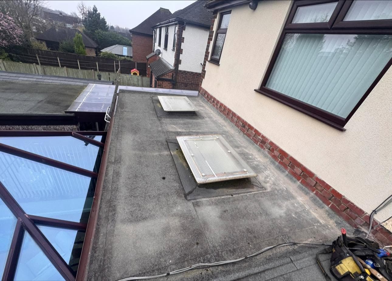 Tired felt flat roof with ageing rooflights before replacement